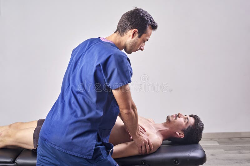 Osteopathy, sports injury rehabilitation concept. A male patient suffering from back pain and a physical therapist. Chiropractic. Shoulder adjustment. Acupressure, man, massage, adult, painful, stretching, caucasian, spanish, medicine, doctor, medical, clinic, mobilization, athletic, sporty, concentrate, muscle, mid, hands, skin, injured, young, soreness, problem, inflammation, cramp, tension, guy, muscular, body, stretcher