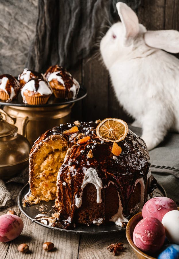 Osterkuchen mit Schokolade und Nüssen auf rustikalem Holztisch mit farbigen Ostereiern und weißem Kaninchen im Hintergrund. frohe stockfoto