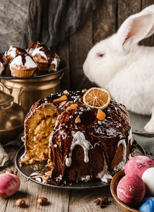 Ostern-Kuchen mit Schokolade und Schalenfrüchten auf rustikalem Holztisch mit farbigen Ostereiern und Weiß Kaninchen auf Hintergru stockbilder