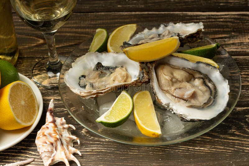 Ostras em uma placa com gelo e limão, com um vidro do vinho seco branco em um fundo de madeira Marisco, restaurante, gosto excele fotos de stock royalty free Ostras em uma placa com gelo e limão, com um vidro do vinho seco branco em um fundo de madeira Marisco, restaurante, gosto excele fotos de stock royalty free