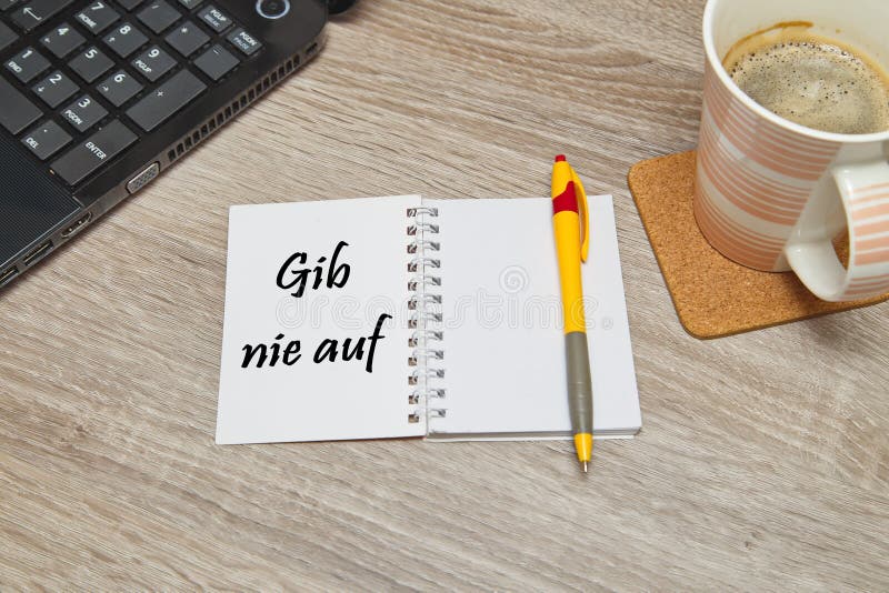 Otwarty notatnik z Niemieckim teksta ` Gib Nie Auf ` Nigdy Daje Up i filiżanka kawy na drewnianym tle