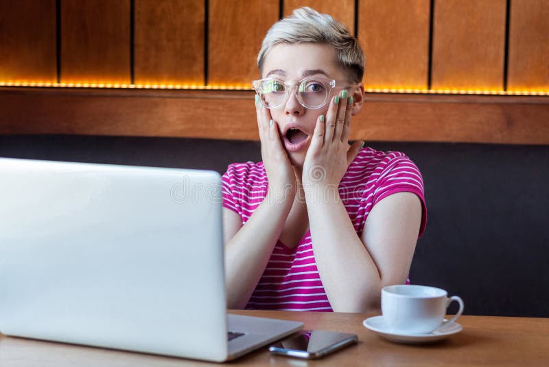 Ouah! Portrait d'une jeune femme d'affaires sous le choc émotionnel en t-shirt rose est assise dans un café, travaillant à dista photo libre de droits