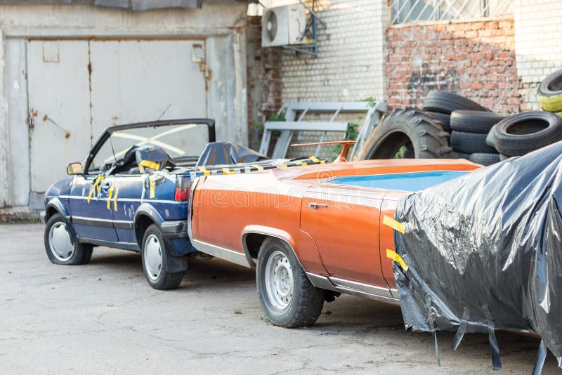 Oude gesloopte behandelde auto bij achtertuin van workshop Verlaten convertibel voertuig onder zwart gordijn dichtbij garagedeure stock foto Oude gesloopte behandelde auto bij achtertuin van workshop Verlaten convertibel voertuig onder zwart gordijn dichtbij garagedeure stock foto