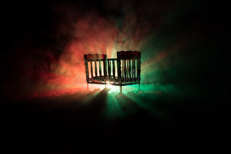 Old creepy eerie wooden baby crib in dark toned foggy background. Horror concept. Scary baby and bed silhouette in dark. Halloween decoration shot. Selective focus. Old creepy eerie wooden baby crib in dark toned foggy background. Horror concept. Scary baby and bed silhouette in dark. Halloween decoration shot. Selective focus