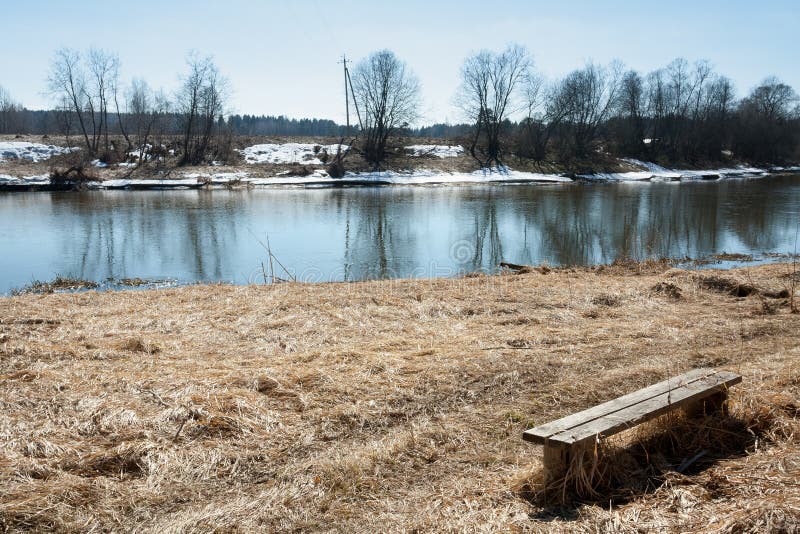 Oude Houten Bank met Haar Schaduw op Droog Gras op Ne van de de Lentekust royalty-vrije stock afbeeldingen Oude Houten Bank met Haar Schaduw op Droog Gras op Ne van de de Lentekust royalty-vrije stock afbeeldingen