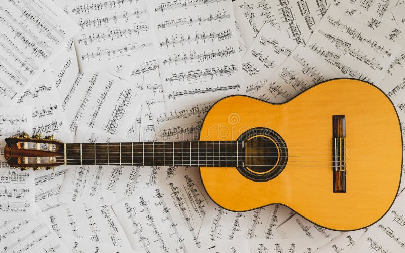 Old yellow classical guitar lying on a pile of sheet music, disoriented musician life. Old yellow classical guitar lying on a pile of sheet music, disoriented musician life