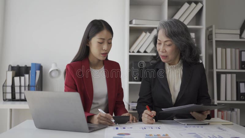 Oudere zakenvrouw en jonge aziatische accountant die het hebben over bedrijfsfinanciën en boekhoudkundige activiteiten op kantoor