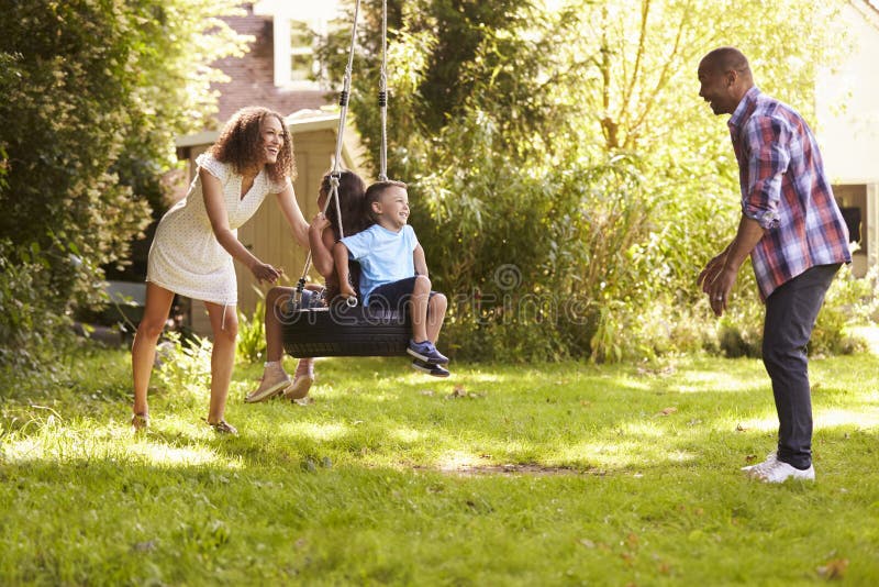 Ouders die Kinderen op Bandschommeling duwen in Tuin stock afbeeldingen Ouders die Kinderen op Bandschommeling duwen in Tuin stock afbeeldingen