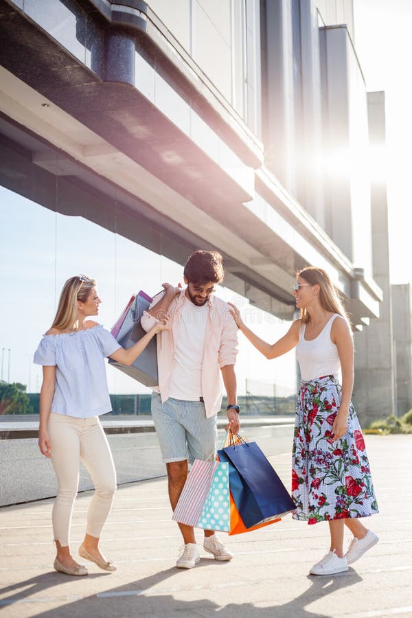 Oungs-Mann, der alle Taschen trägt, während zwei Freundinnen sind, scherzend lachend und durch seine Seite stockfotos Oungs-Mann, der alle Taschen trägt, während zwei Freundinnen sind, scherzend lachend und durch seine Seite stockfotos