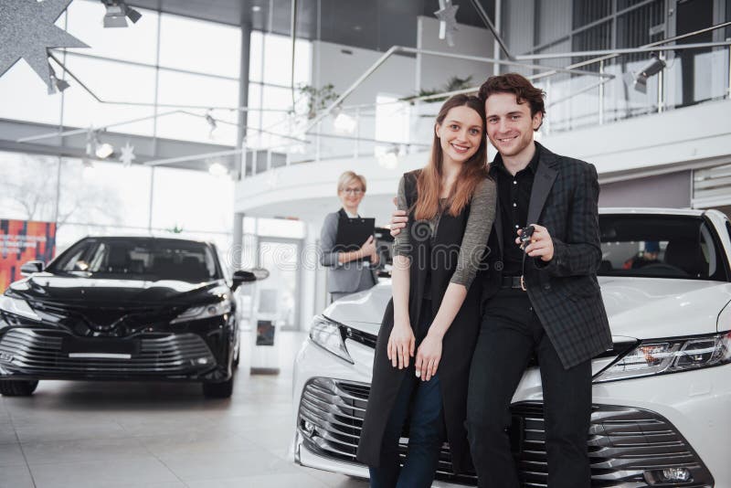 Our first car. Beautiful happy woman smiling showing the keys to a new car they just bought with her husband happy stock photos Our first car. Beautiful happy woman smiling showing the keys to a new car they just bought with her husband happy stock photos