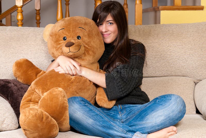 Ours de nounours d'embrassement de jeune femme se reposant sur le sofa photo stock Ours de nounours d'embrassement de jeune femme se reposant sur le sofa photo stock