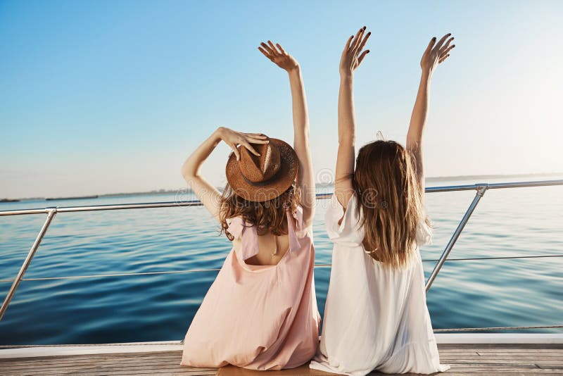 Outdoor back shot of two young female on luxury vacation, waving at seaside while sitting on yacht. Best friends are royalty free stock photos Outdoor back shot of two young female on luxury vacation, waving at seaside while sitting on yacht. Best friends are royalty free stock photos