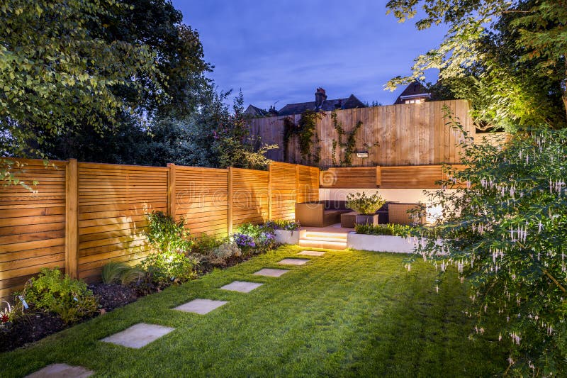 Cortile recintato con terrazza patio e mobili da giardino illuminato di sera.