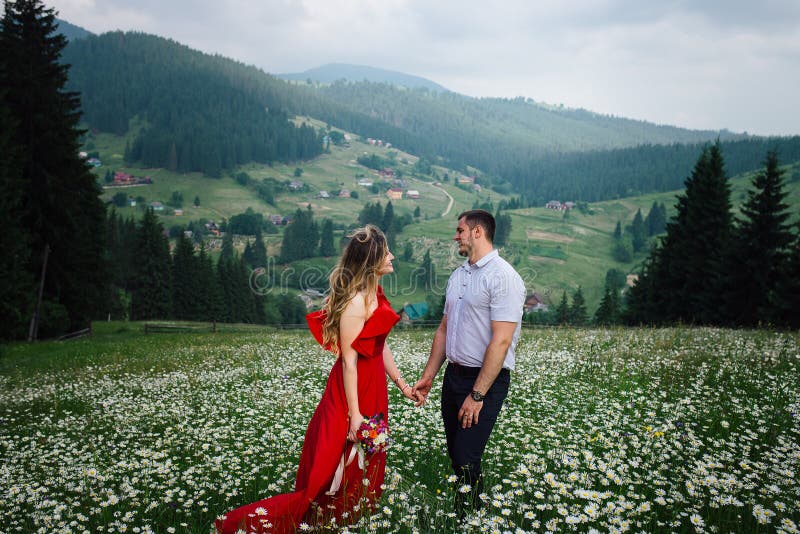 Outdoor portrait of the attractive smiling couple holding hands on the daisy meadow at the background of the beautiful stock photos Outdoor portrait of the attractive smiling couple holding hands on the daisy meadow at the background of the beautiful stock photos