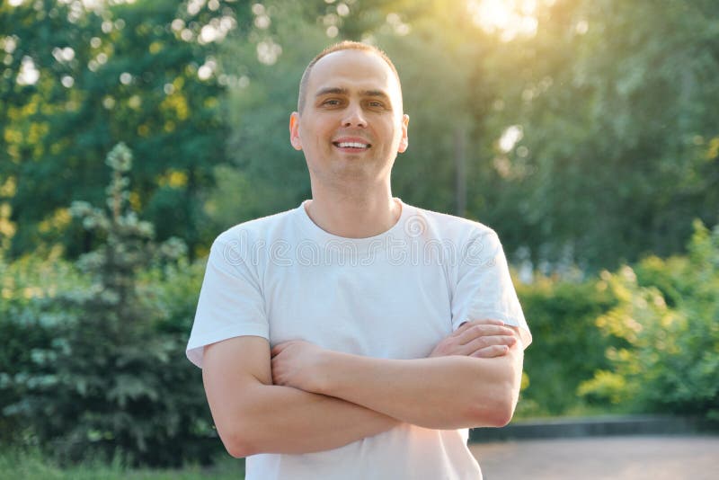 Outdoor portrait of confident smiling middle-aged sports man. Positive handsome male with arms crossed in white t-shirt looking at royalty free stock photos Outdoor portrait of confident smiling middle-aged sports man. Positive handsome male with arms crossed in white t-shirt looking at royalty free stock photos