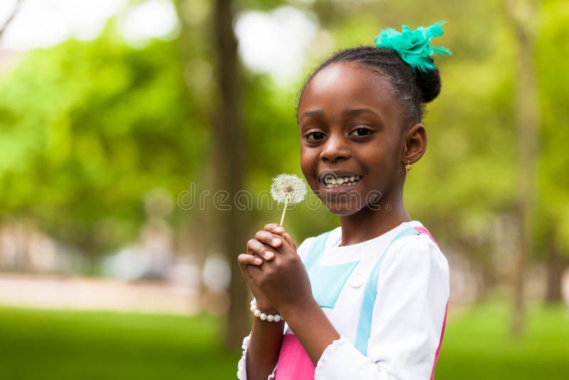 Outdoor portrait of a cute young black girl holding a dandelion