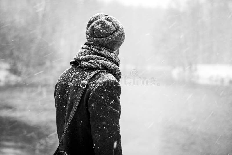 Outdoor portrait of handsome young man in snowy winter forest. Snowfall. Guy looking away on frozen river. Black and white