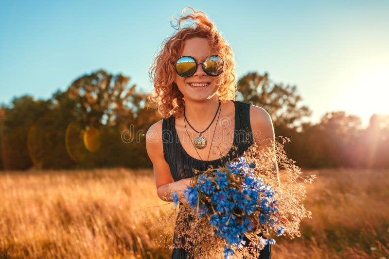 Outdoor portrait of happy young woman with red curly hair holding flowers. Summer holidays.