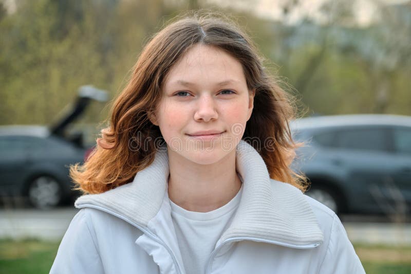 Outdoor portrait of teenager girl 15 years old, girl smiling with long brown hair in white jacket