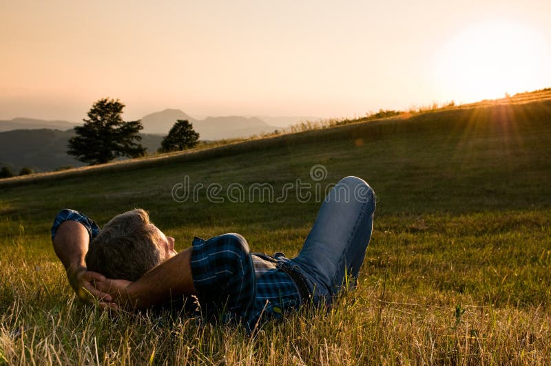 Uomo maturo per una pausa e rilassarsi in un prato in una splendida luce calda del tramonto.