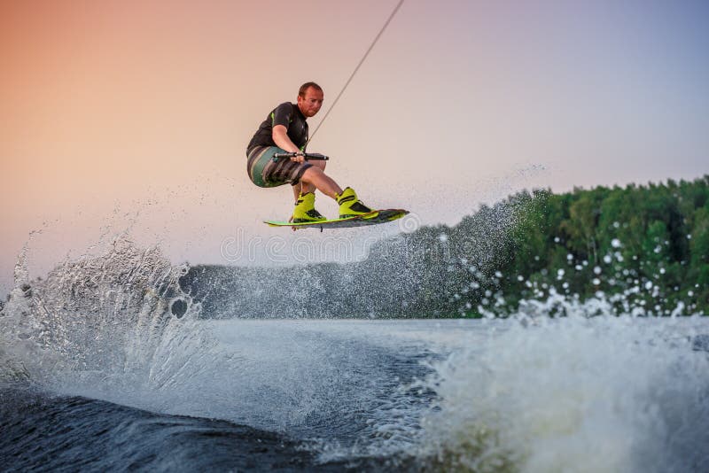 Wakeboard rider making tricks on a lake at orange sunset. Outdoor shot of action man wakeboarding and jumping tricks on a lake at orange sunset, extreme sport stock image Wakeboard rider making tricks on a lake at orange sunset. Outdoor shot of action man wakeboarding and jumping tricks on a lake at orange sunset, extreme sport stock image