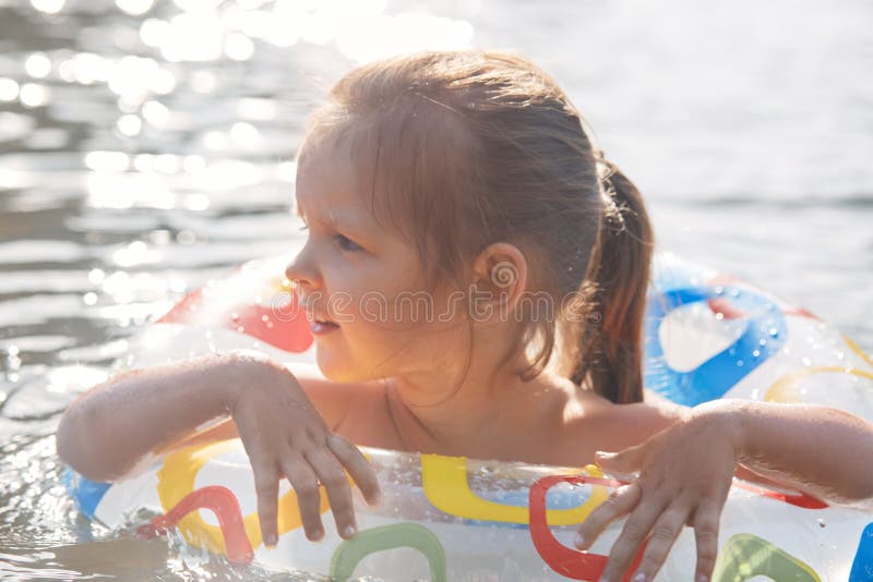 Outdoor shot of fair haired funny little girl spending free time in lake, learning to swim with swimming circle, looking aside, stock photos Outdoor shot of fair haired funny little girl spending free time in lake, learning to swim with swimming circle, looking aside, stock photos