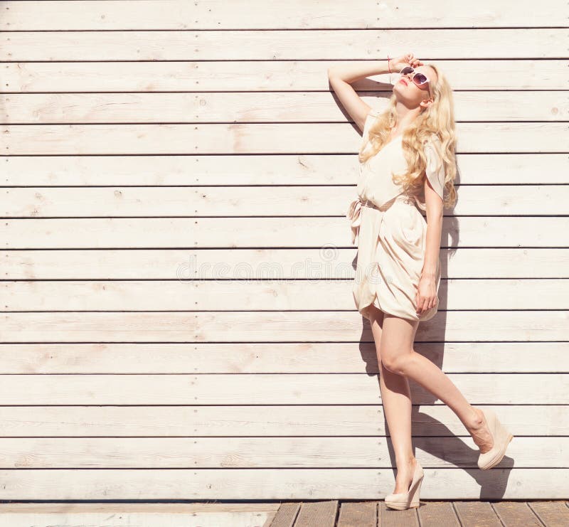 Outdoor summer sensual fashion portrait beautiful young blond woman a white dress standing on the background of wooden planks. Ton