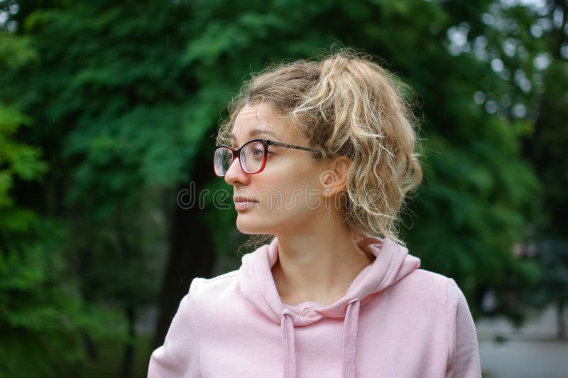 Outdoorportrait eines jungen Mädchens mit blonden Haaren in rosa Pullover mit Hipster-Brille im Park lizenzfreies stockbild Outdoorportrait eines jungen Mädchens mit blonden Haaren in rosa Pullover mit Hipster-Brille im Park lizenzfreies stockbild