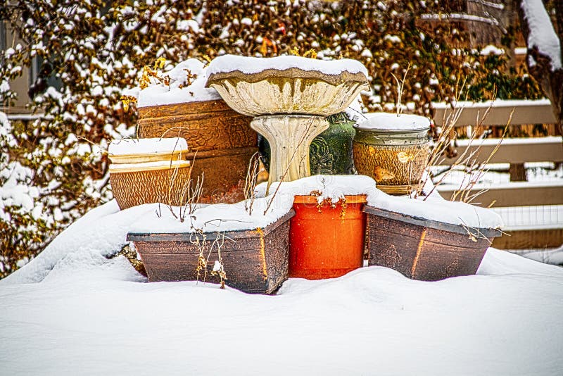 Outside flower pots  with dead plants stacked around concrete bird feeder in winter partly covered with snow