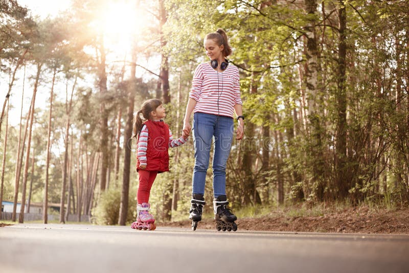 Outside picture of pleasant tender sweet young female having rest with her little daughter, holding her hand, teaching to stock images Outside picture of pleasant tender sweet young female having rest with her little daughter, holding her hand, teaching to stock images