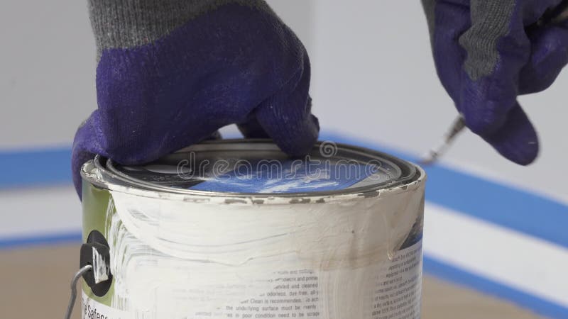 Ouverture enfilée de gants de main une boîte de peinture blanche avec l'ouvre-boîte avant de commencer une salle de peinture