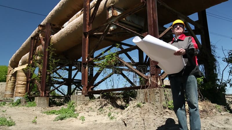 Ouvrier dans le casque antichoc jaune avec des dessins de projet à la centrale de la chaleur