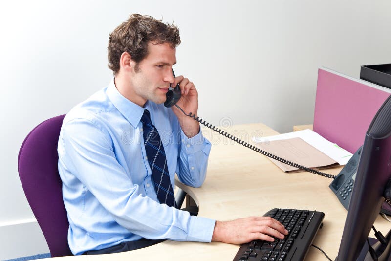 A male office worker answering the phone and looking at a computer monitor in a customer service centre. A male office worker answering the phone and looking at a computer monitor in a customer service centre.