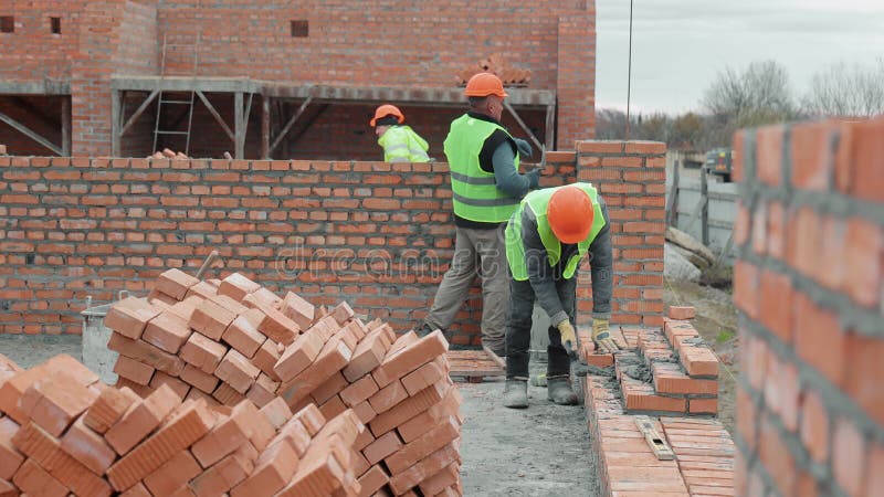 Ouvriers du bâtiment ponte des briques sur chantier. Deux ouvriers de la construction dans des gilets réfléchissants et des chapea banque de vidéos