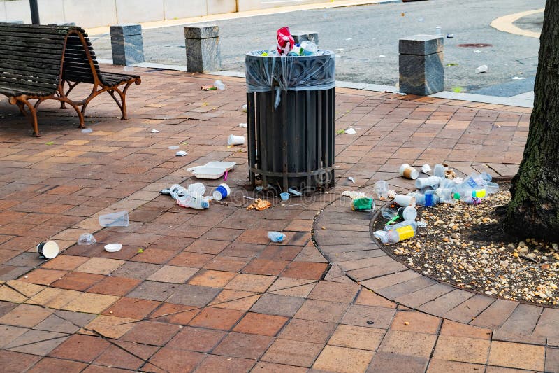Overflowing Trash Can on City Sidewalk Surrounded by Scattered Litter, Cups and Plastic Waste royalty free stock image