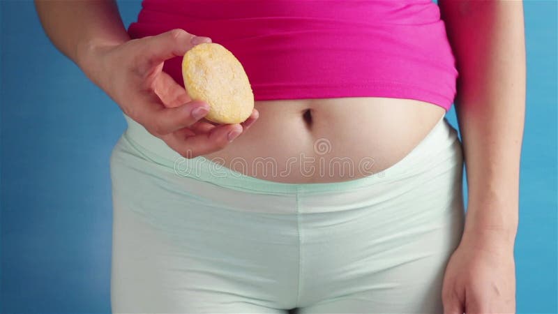 Overgewicht vrouw met dikke buik die koekje vasthoudt en duim omhoog laat zien