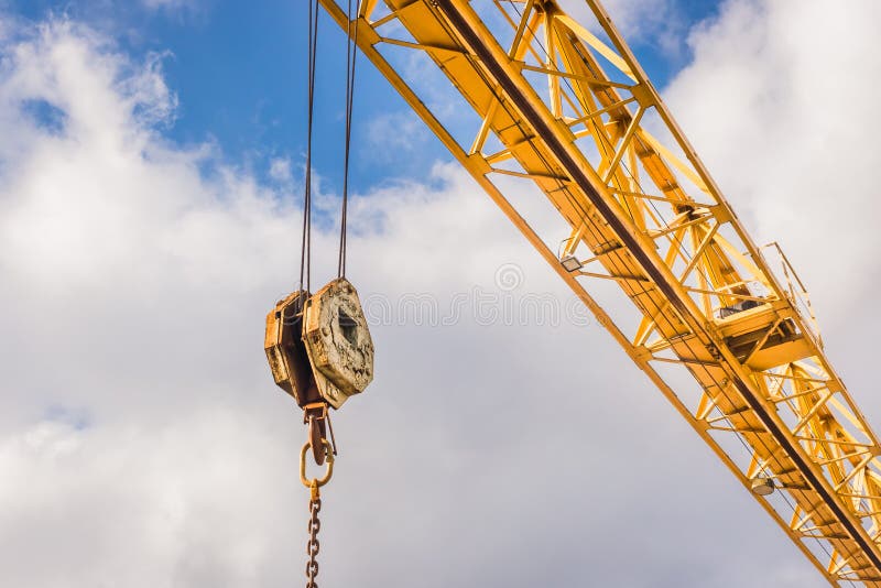 Overhead crane hoist industrial mechanism with hook and chain on a background of blue sky with clouds, close-up