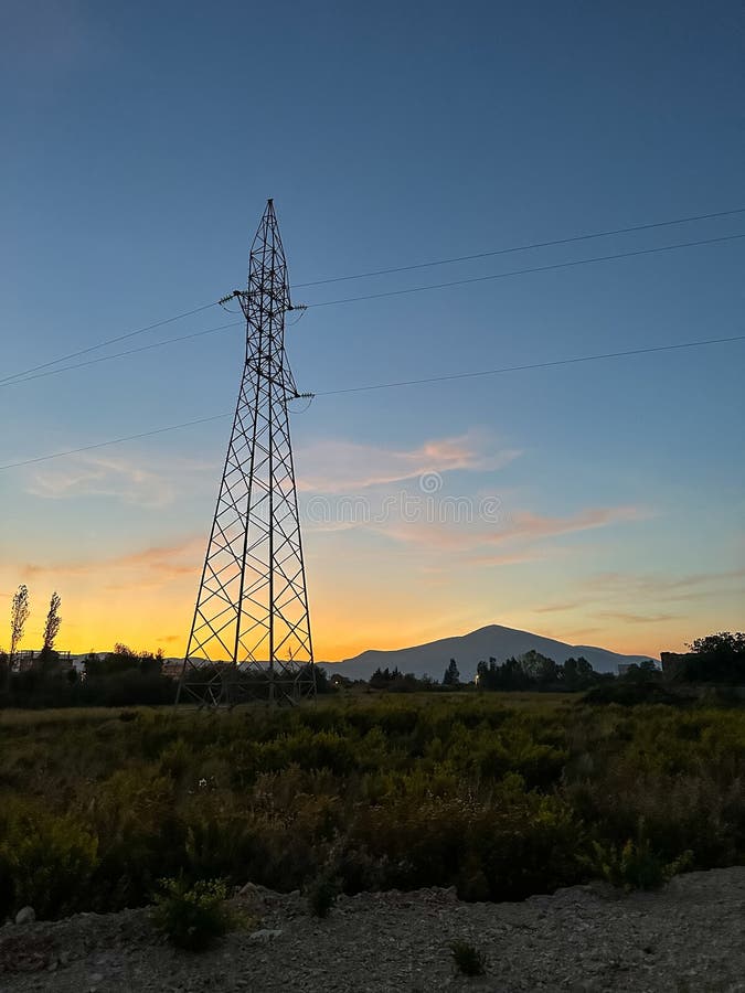 Overhead line pylons, high voltage pylons in meadow with mountains on background stock image