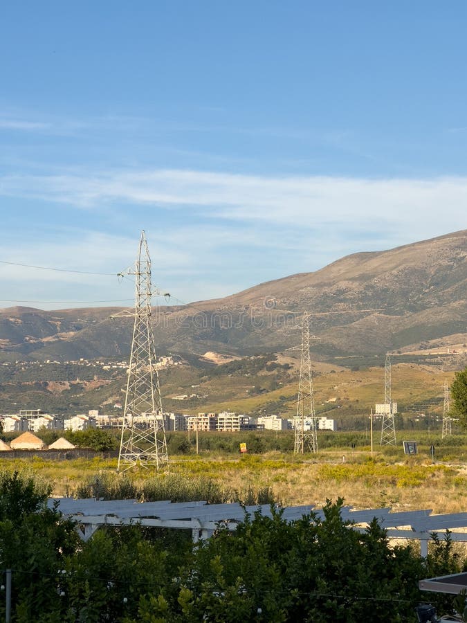 Overhead line pylons, high voltage pylons in meadow with mountains on background stock photography