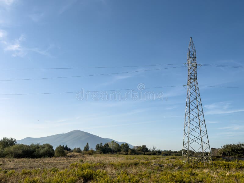 Overhead line pylons, high voltage pylons in meadow with mountains on background royalty free stock photography