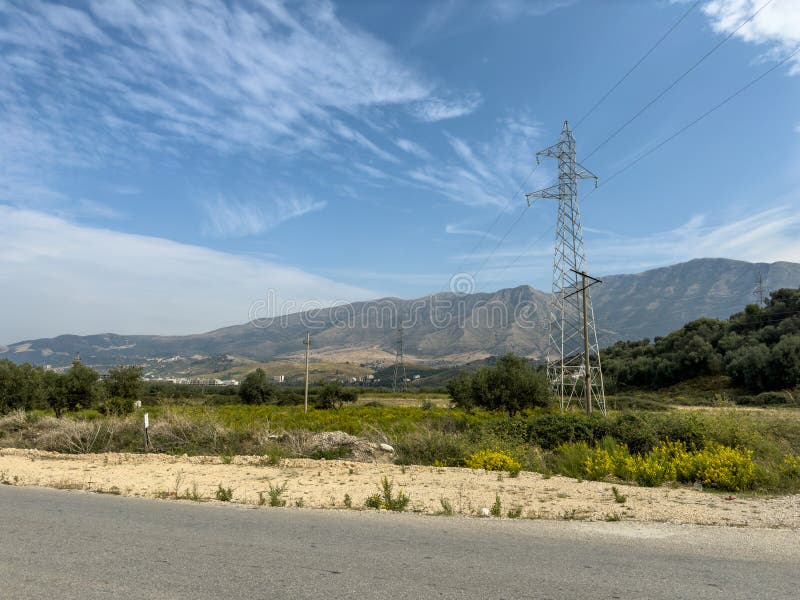 Overhead line pylons, high voltage pylons in meadow with mountains on background stock photo