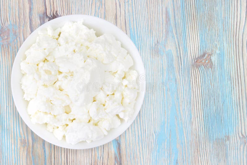 An overhead photo of fresh natural cottage cheese in a white ceramic bowl on the wooden table. Organic eco healthy meal, dairy stock image An overhead photo of fresh natural cottage cheese in a white ceramic bowl on the wooden table. Organic eco healthy meal, dairy stock image