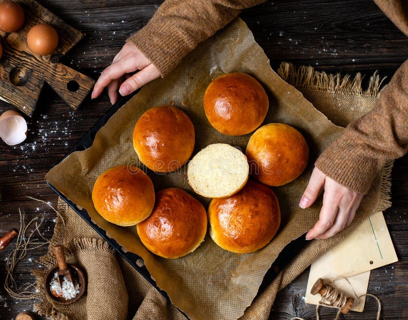 Overhead shot of homemade cut baked burger buns on baking tray with parchment in woman hands