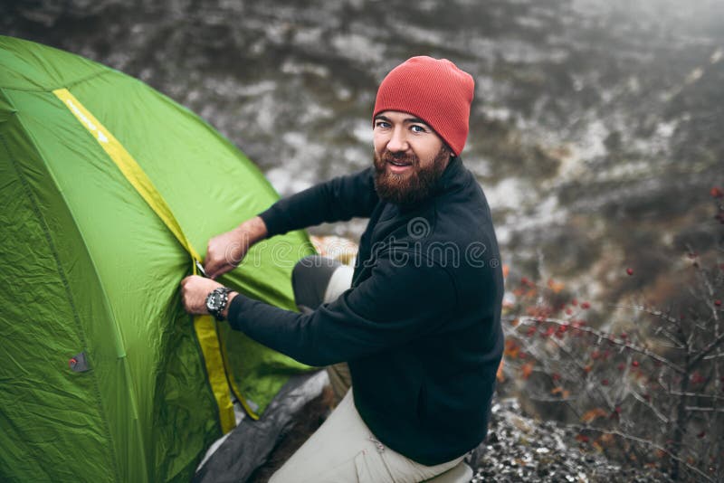 Overhead shot of traveler man with beard pitch tent camping gear outdoor in mountain. Male hiking in moutain. Travel, lifestyle