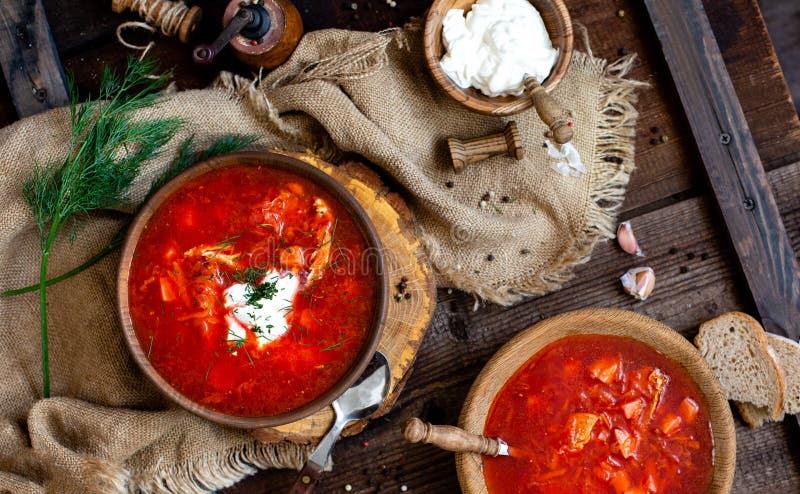 Overhead shot of two wooden bowls with tasty Ukrainian or Russian traditional beetroot soup borscht with sour cream