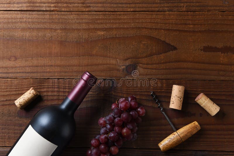 Overhead view of a Cabernet Sauvignon wine bottle on a dark wood surface with grapes and cork screw corks and copy space