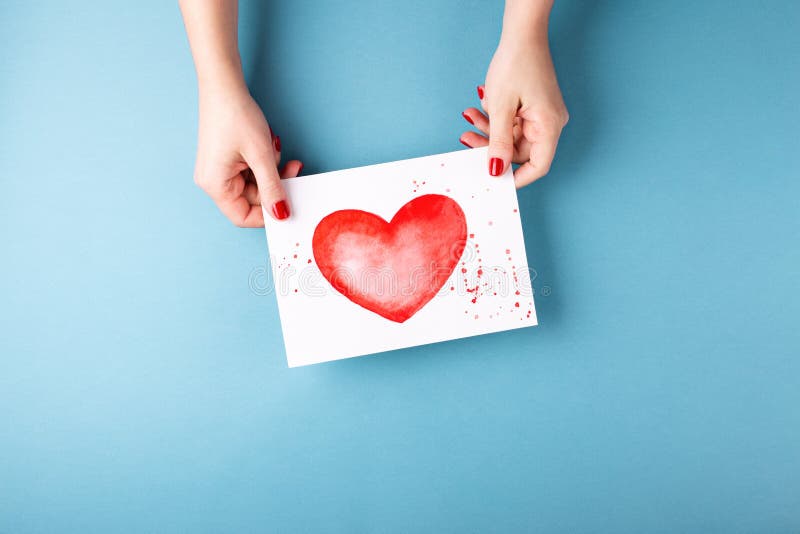 Female hands holding card with heart on blue background. stock photo