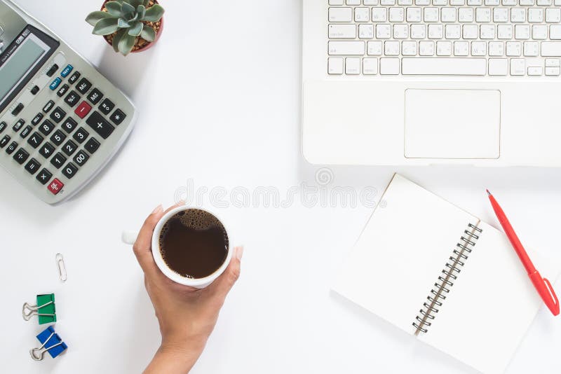 Overhead view of woman hand holding cup of coffee with laptop and calculator on white background, Work space and accouting concept