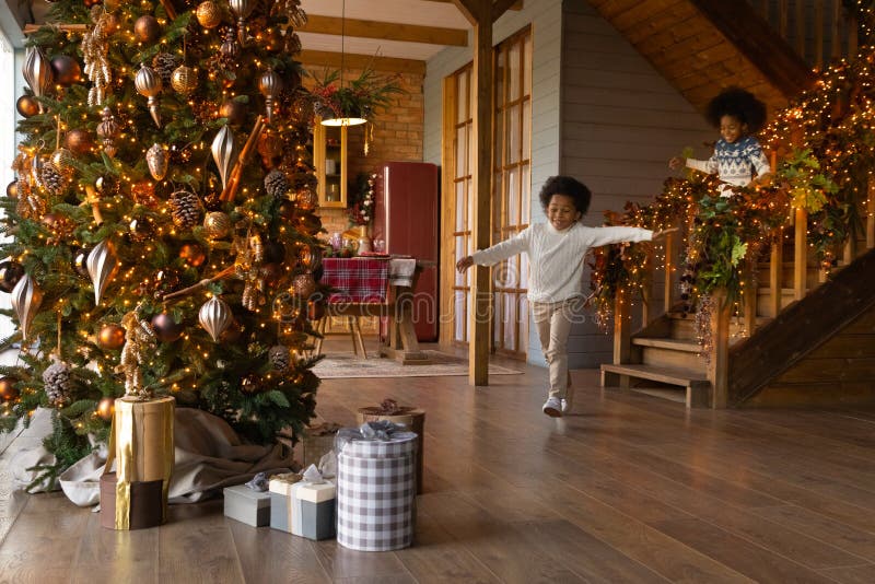 Overjoyed African American little kids wearing sweaters running downstairs on Christmas morning to opening presents, gift boxes under decorated festive tree, excited girl and boy celebrating New Year. Overjoyed African American little kids wearing sweaters running downstairs on Christmas morning to opening presents, gift boxes under decorated festive tree, excited girl and boy celebrating New Year