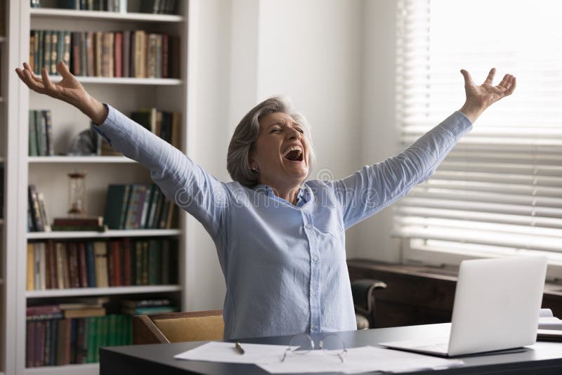 Overjoyed happy middle aged 60s woman screaming with raise in air arms, getting email with amazing news, celebrating online lottery gambling win, getting bank loan approval, internet success. Overjoyed happy middle aged 60s woman screaming with raise in air arms, getting email with amazing news, celebrating online lottery gambling win, getting bank loan approval, internet success.